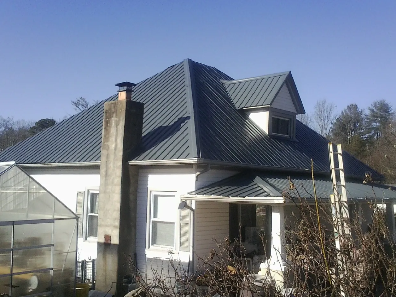 Dark blue standing seam metal roof on a white farmhouse with dormer — Slate & Tile Roof Repair by Roofing Brothers in Katonah