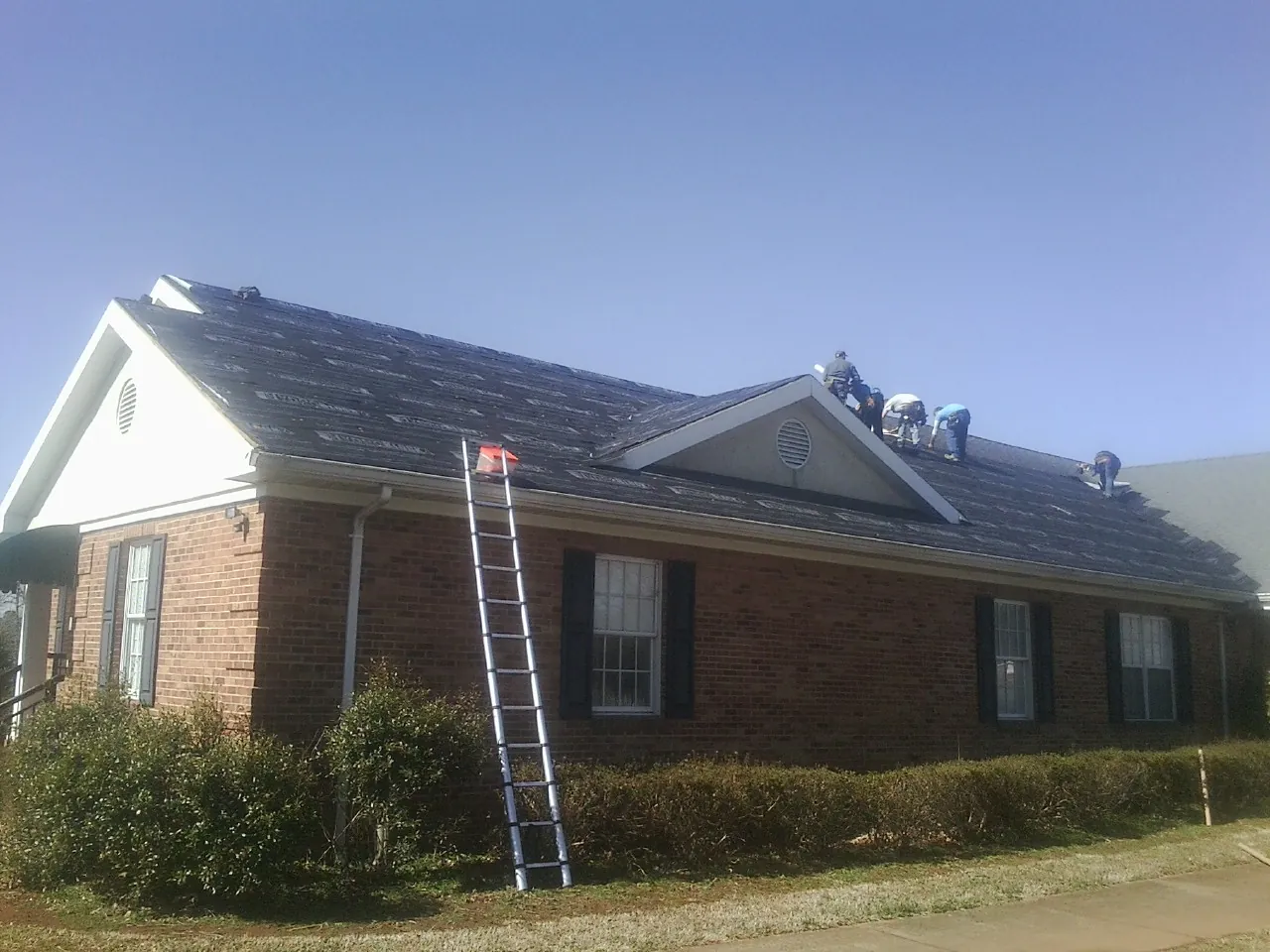 Crew tearing shingles off a brick ranch roof with a ladder set — Emergency Roof Repair work by our crew in Katonah