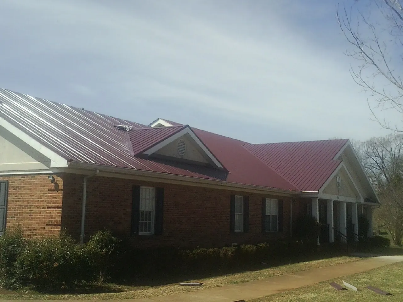 Red metal roof with gabled entries on a long brick building, from a Hail Damage Roof Repair job in Katonah