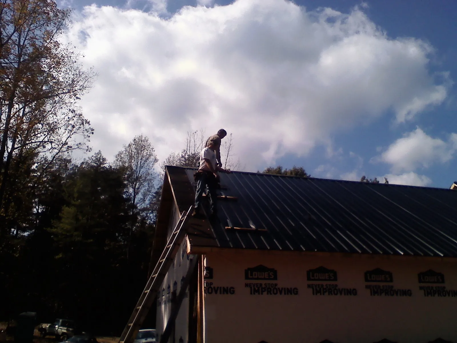 Roofer fastening dark metal panels high against a cloudy sky, from a Roof Inspection job in Katonah