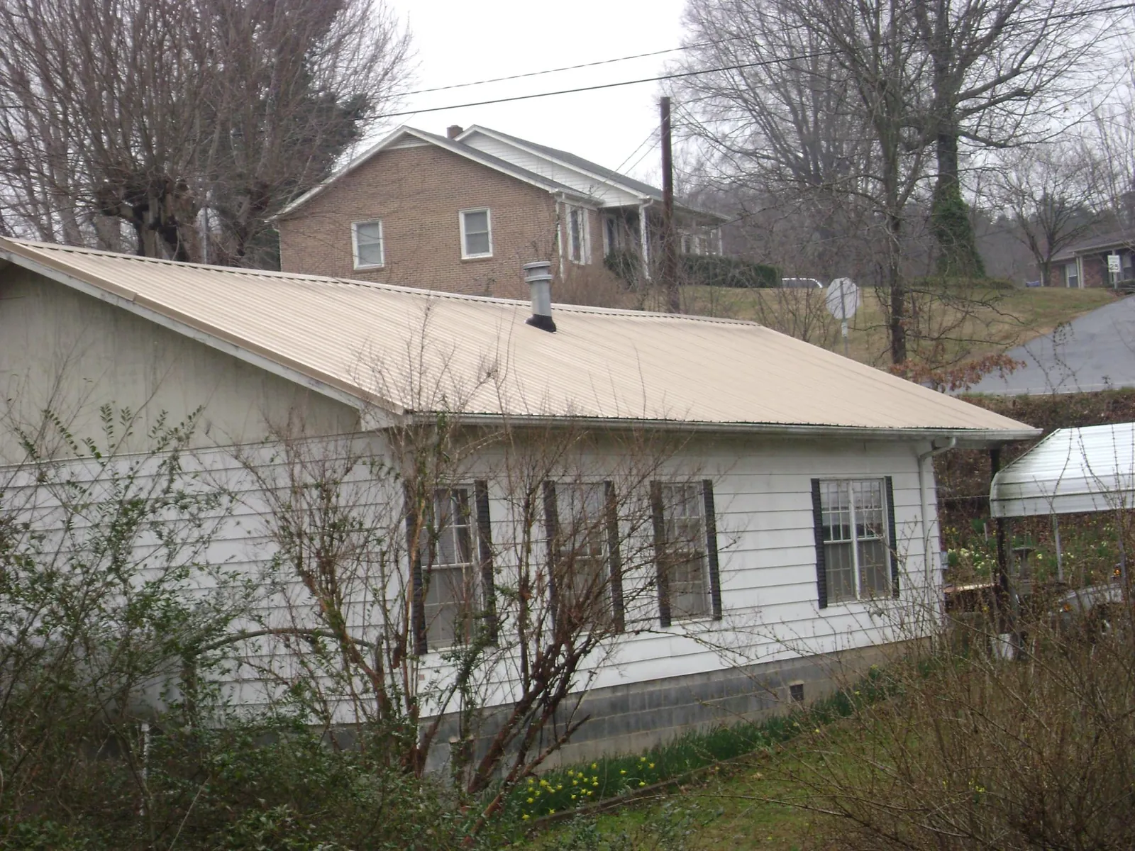 Tan metal roof on a white sided house set into a hillside — Commercial Roofing by Roofing Brothers in Katonah